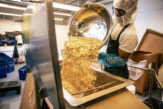 A Naturalvert baker pouring granola from a steel bowl into a mixer in our Hawthorne, New Jersey kitchen